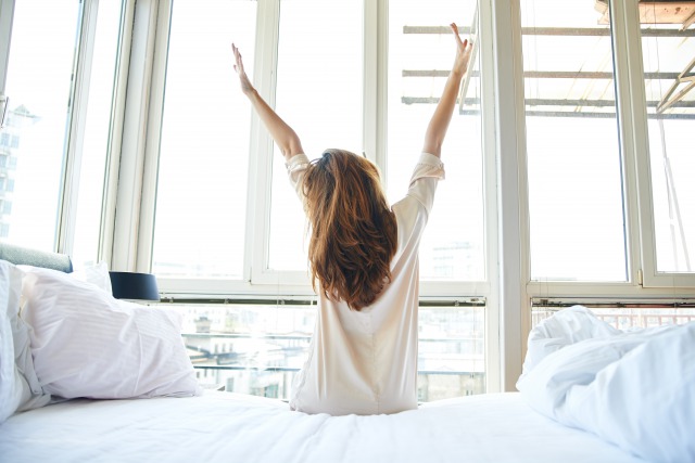 朝にベッド上で手を挙げる女性